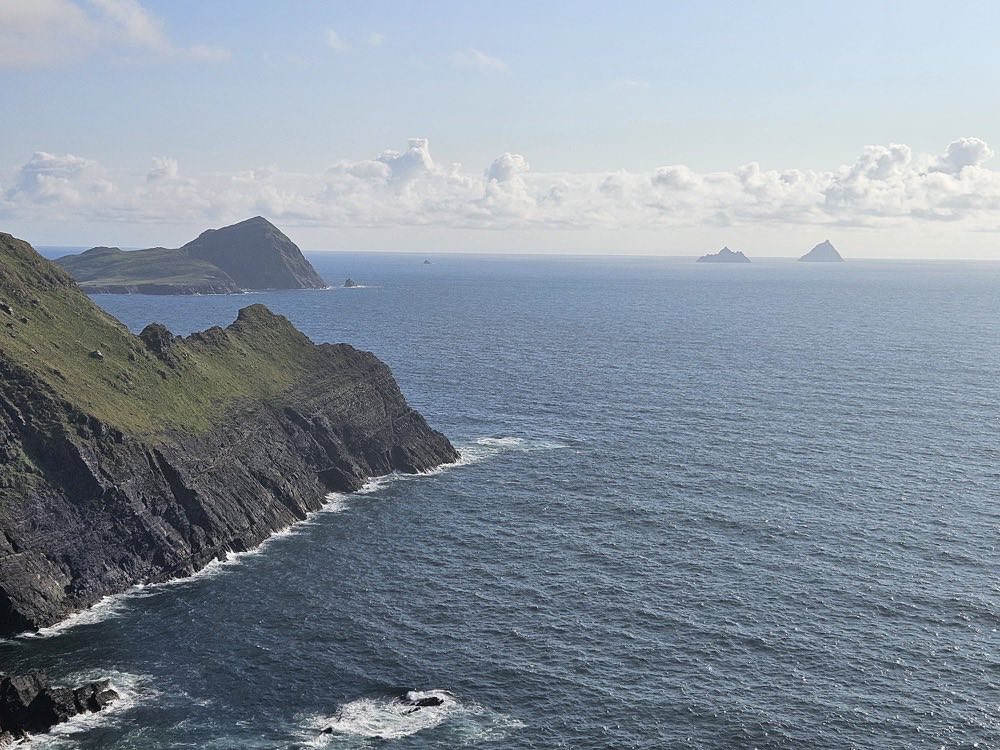A headland of green-topped sea cliffs with the Skellig Islands on the horizon
