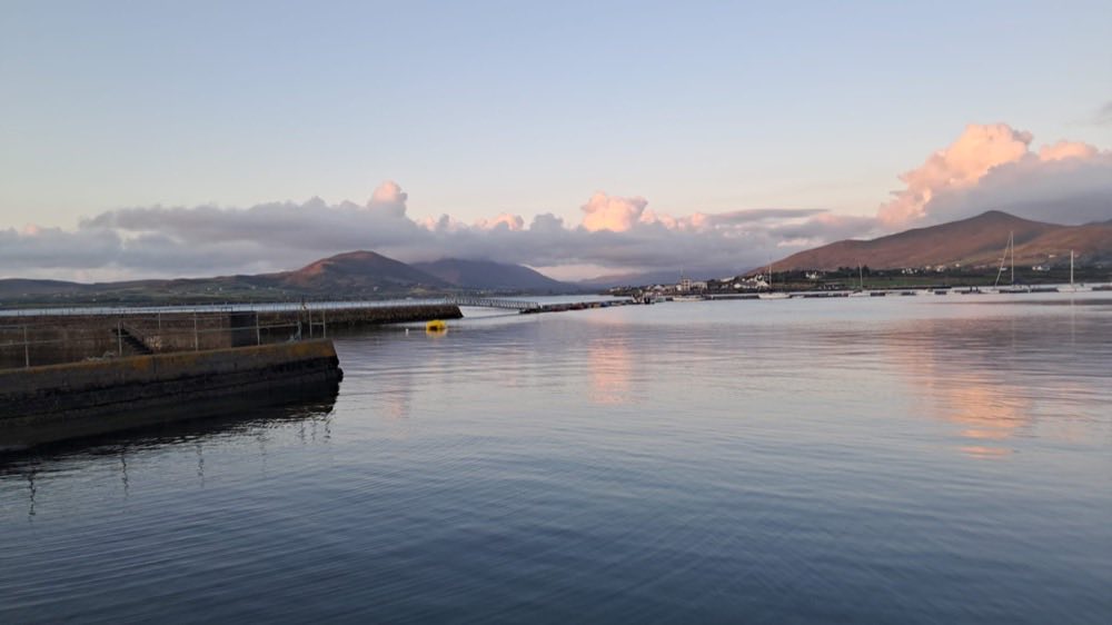 Still water and a stone pier at a west of Ireland harbour in soft evening light