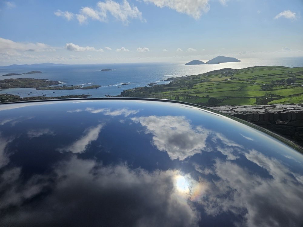 Sky and cloud reflected in the polished roof of the car above a bay of green islands on the Ring of Kerry